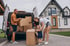 Eine junge Familie belädt beim Umzug einen Transporter mit Kartons vor einem modernen Einfamilienhaus.