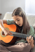 A young girl with long brown hair plays an acoustic guitar, strumming the strings with her right hand.