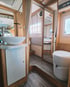 Badezimmer in einem Wohnmobil mit ovalem Waschbecken, Toilette und Holzmöbeln.