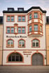 Weiße Fassade eines Gebäudes mit der Aufschrift „Deutsches Haus.“ und „SKOPELOS Restaurant“, mit Erker und Statue.