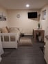 Ein gemütliches, kleines Zimmer mit Bett, Tisch, Teppich, Fernseher und Wanduhr, alles in neutralen Farbtönen.