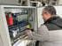 Ein Techniker mit Brille arbeitet an einem offenen Schaltschrank mit roten und grauen Modulen und vielen Kabeln.