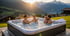 Familie genießt einen Whirlpool im Freien bei Sonnenuntergang vor einer Bergkulisse.