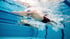 Zwei Schwimmer in Badekappen und Brillen schwimmen unter Wasser im Schwimmbecken.