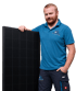 Ein Mitarbeiter in blauer Berufsbekleidung der Firma Herner steht lächelnd neben einem schwarzen Solarmodul.