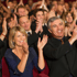 Lächelndes Publikum in einem Theater, das in roten Sitzen sitzt und applaudiert.