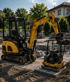 Gelber Minibagger und eine Rüttelplatte auf einer Baustelle vor einem Wohnhaus.
