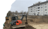 Bagger auf einer Baustelle mit einem ausgehobenen Fundament vor einem Wohnhaus.