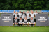 Zwei Reihen von Fußballern und Trainern in grauen Trikots vor Bannern mit der Aufschrift "TSA TORWARTCAMP ENNIGERLOH".