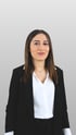 Beyza Yildirim, professionelles Business-Porträt einer Frau mit dunklen Haaren im schwarzen Blazer und weißer Bluse vor neutralem grauen Hintergrund.