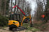 Gelber JCB Minibagger und roter Holzkran bei Forstarbeiten an einer Waldstraße mit einem Waldarbeiter in Warnweste.