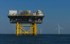 Gelbe Offshore-Plattform mit Windturbinen im Meer unter blauem Himmel.