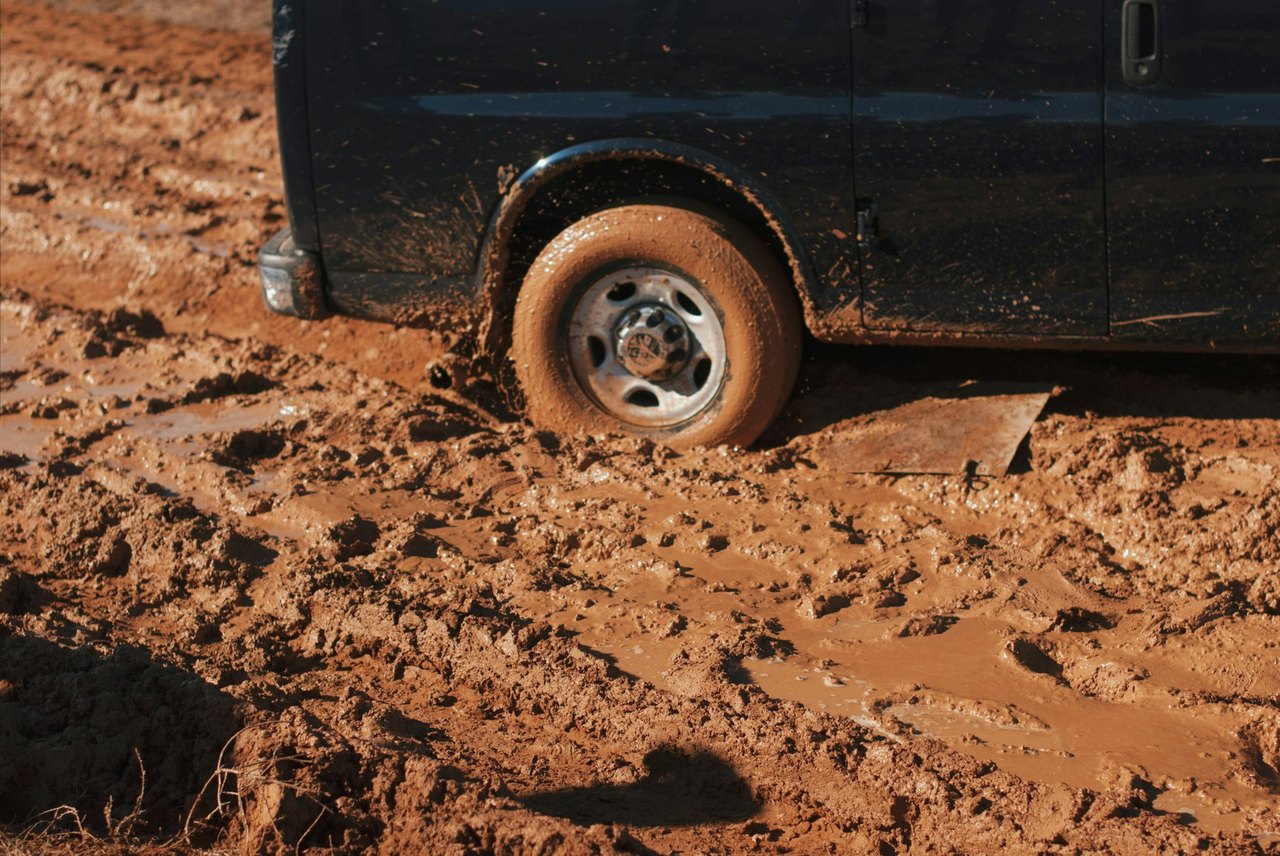 Vehicle stuck in mud with a wheel sunk past the rim, the kind of recovery job seen on farm roads around Hanford, California