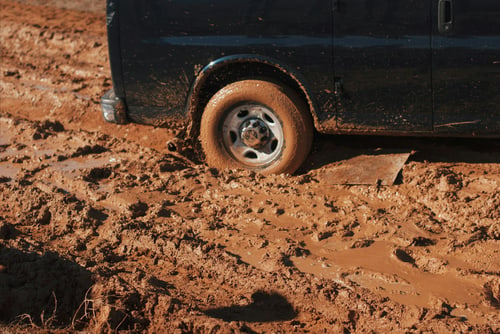 Vehicle stuck in mud with a wheel sunk past the rim, the kind of recovery job seen on farm roads around Hanford, California