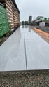 Frisch verlegte, großformatige hellgraue Terrassenplatten in Steinoptik auf einem Kiesbett neben einer Holzfassade.