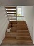 Moderne Holztreppe mit zwei Abschnitten, Glasgeländer und einem Kissen auf der unteren Stufe.