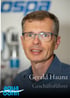 Gerald Haunz, Geschäftsführer, trägt eine blaue Hemd und Brille vor einem unscharfen Hintergrund mit "ospa" und "aqua bonn" Logos.