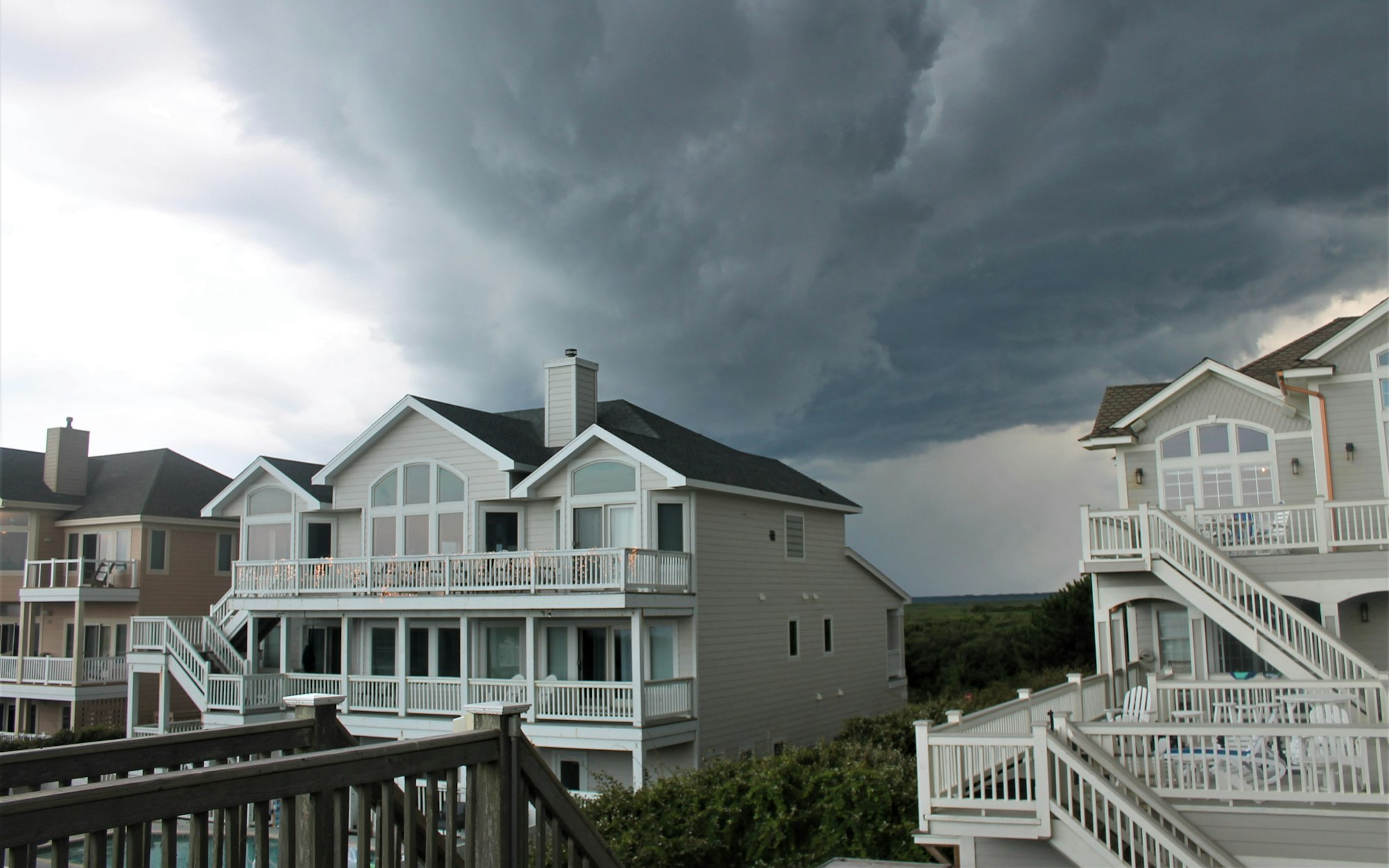 Storm clouds rolling in over a row of shingle-roofed houses, the kind of straight-line wind that causes wind damage to roof shingles around Sherman