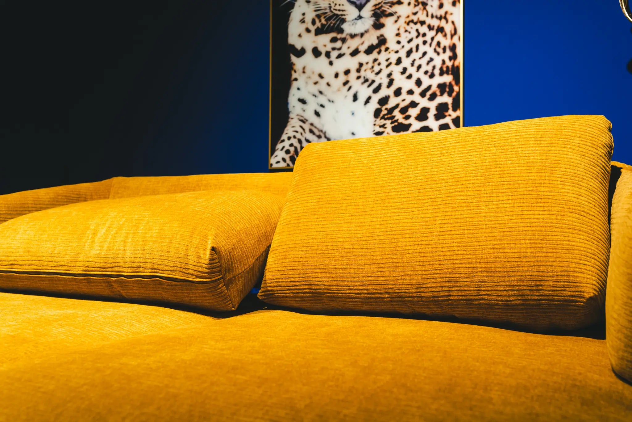 Senfgelbes Cord-Sofa vor blauer Wand mit Leoparden-Wandbild
