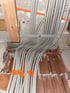 Graue Elektrokabel sind an einer Holzleiste und mit orangefarbenen Clips an einer Ziegelwand befestigt.