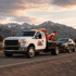 Towing Sandy wrecker truck transporting a sedan along a mountain highway in Sandy, Utah.