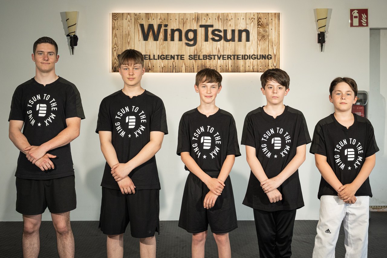 Fünf Jugendliche im Trainingsshirt vor dem WingTsun-Schild