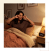 A woman sits in bed rubbing her eyes next to a digital alarm clock displaying 3:47 AM under a warm bedside lamp.