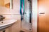 Kleines Badezimmer mit weißer Fliesenwand, Waschbecken, Duschkabine mit blauem Duschvorhang und Holztür.