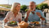 Ein lächelndes älteres Paar isst im Freien auf einer Restaurantterrasse mit Salaten und Brot.