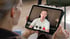 Frau hält ein Tablet und führt ein Videotelefonat mit einem Mann in einem weißen Poloshirt.