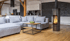 Geräumiges Wohnzimmer mit grauem Sofa, Holzboden und Kaminofen vor einer dunklen Ziegelwand.