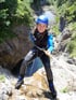 Eine lächelnde Frau beim Canyoning, die sich an einem Seil einen Felsen hinunter abseilt.