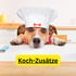 Hund mit Kochmütze und rotem Halstuch blickt über eine Theke; "Koch-Zusätze" in Gelb.