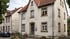 Zweistöckiges Wohnhaus mit heller Fassade, Satteldach und blauer Eingangstür in einer bewohnten Straße.