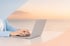 Hände tippen auf einem silbernen Laptop vor einem Hintergrund mit Meer und Sonnenuntergang.