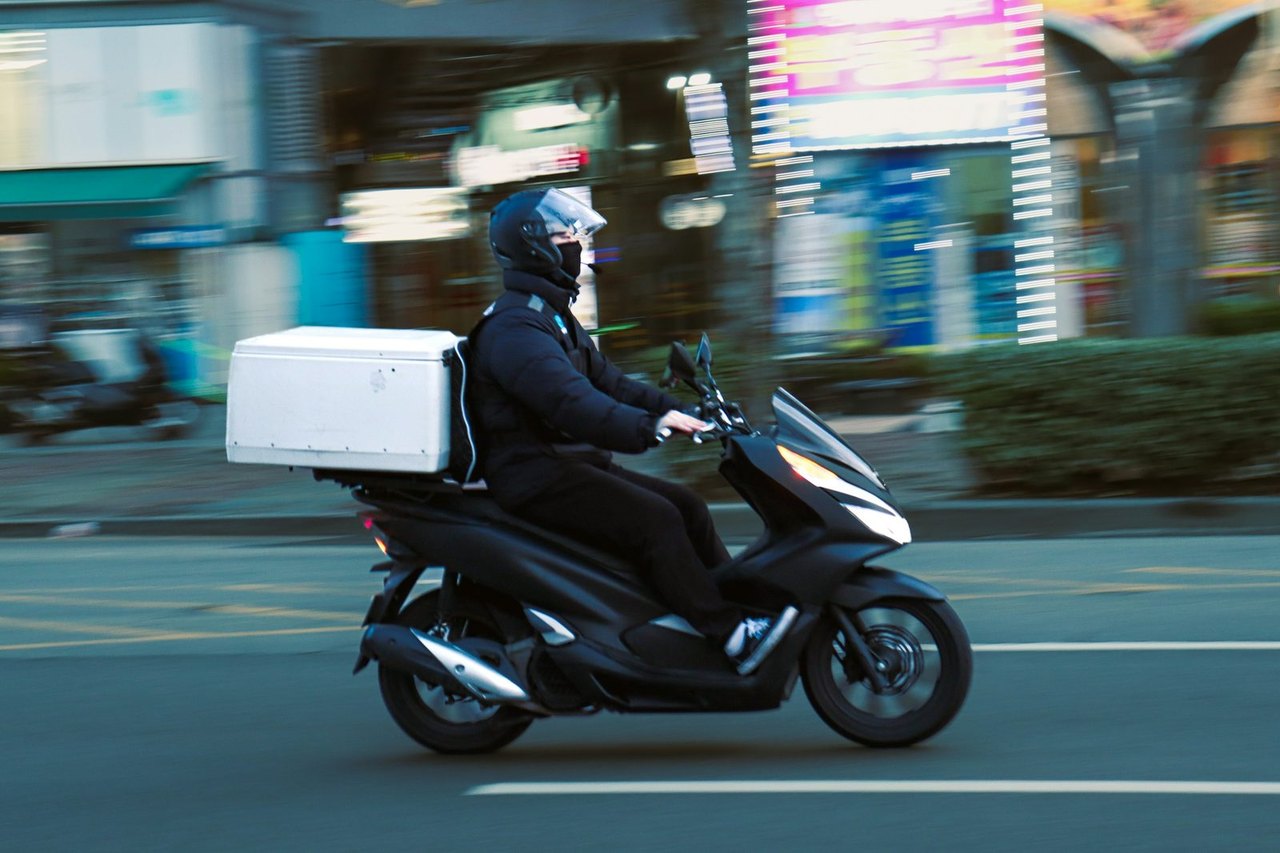 Kurier auf einem Motorroller mit Transportbox fährt durch die Stadt