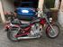 Rotes und schwarzes Motorrad mit Windschutzscheibe und Chromdetails, geparkt vor einer Garage mit blauem SUV.