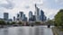 Skyline von Frankfurt am Main mit Wolkenkratzern am Mainufer und dem Eisernen Steg unter bewölktem Himmel.