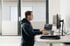 Zwei Männer sitzen in einem modernen Büro und arbeiten an Computern, schwarze Thermoskanne auf dem Schreibtisch.