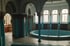 Verlassenes Badezimmer mit rundem Becken, blauen Fliesen, Säulen und Bogenfenstern.