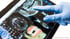 Eine Hand mit blauem Handschuh tippt auf einen Tablet-Bildschirm mit 3D-Zahnröntgenbildern.