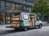 Ein weißer Lieferwagen mit geöffneten Seiten- und Hecktüren, gefüllt mit Holzkisten voller Obst und Gemüse.