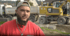 Junger Mann in rotem T-Shirt mit „rossaro Baugruppe“-Logo, im Hintergrund eine Straßenwalze.