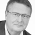 Ein lächelnder Mann mit kurzen Haaren und Brille blickt nach vorne und trägt ein Hemd mit Kragen.