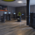 Ein Fitnessstudio mit mehreren Trainingsgeräten, Holzboden und einer grünen Pflanze auf einem schwarzen Fass.