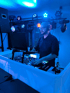 DJ mit Kopfhörern und Laptop an einem Mischpult unter blauen Lichtern.