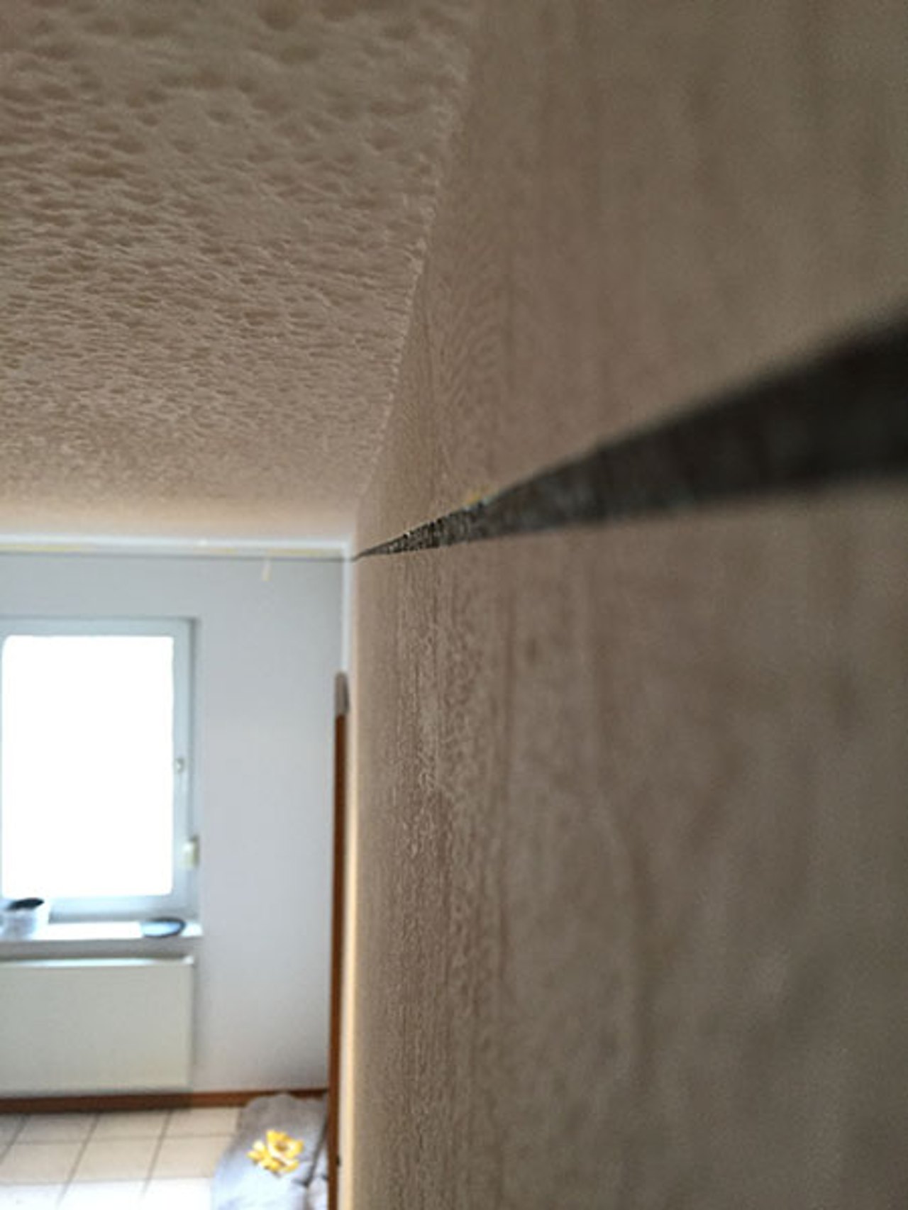 Ein langer, horizontaler Strich verläuft durch die Raufasertapete an einer Innenwand unterhalb der Decke.