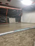 Frisch gegossener Betonboden in einem Raum, dessen Wände teilweise mit schwarzer Folie und orangefarbenem Klebeband abgedeckt sind.