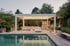 Moderne Terrassenüberdachung über einer Sitzecke mit Außenküche und Pool bei Dämmerung.