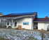 Haus mit roten Ziegeln und Photovoltaik-Paneelen auf dem Dach, teilweise schneebedeckter Vorgarten.